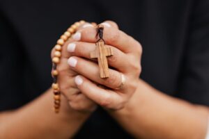 A detailed close-up of hands clasping a wooden rosary with cross, symbolizing faith.