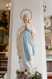 A serene statue of the Virgin Mary with a rosary, praying inside a beautiful church.